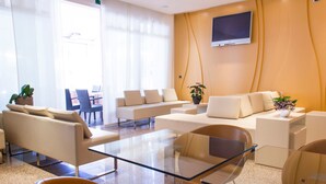 Un área de espera moderna con sofás, sillas, una mesa de vidrio y una televisión en la pared.