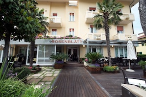 Entrada de hotel con terraza de madera, asientos al aire libre y un cartel que dice "ROSENBLATT".