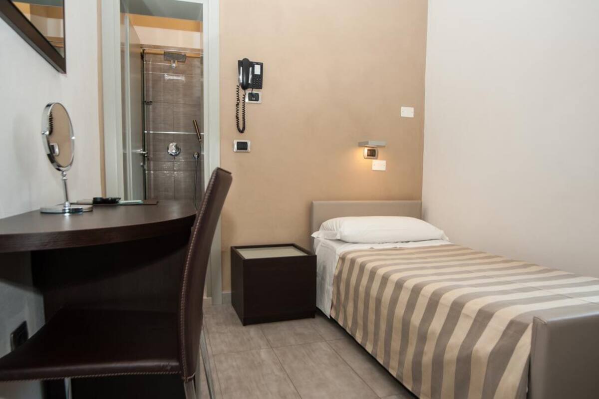 A small hotel room with a desk, chair, bed, and a shower area.