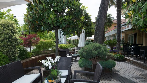 Un patio exterior con mobiliario de mimbre, una mesa con bebidas y un letrero que dice 'Rosenblut'.