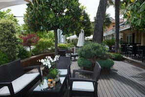 An outdoor patio area with wicker furniture, a table with drinks, and a sign for 'Rosenblut'. - Hotel Rosenblatt (Cervia)