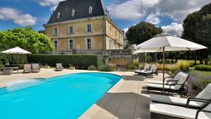 A swimming pool with lounge chairs and umbrellas, a large building with a dark roof, and a well-maintained garden. - Château de Villars (Villars)