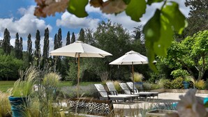 A poolside area with lounge chairs and umbrellas, surrounded by lush greenery and tall trees. - Château de Villars (Villars)