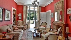 A room with a red wall, a fireplace, a chandelier, and a large window. - Château de Villars (Villars)