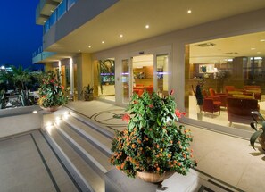 Vestíbulo de hotel con diseño moderno, que presenta una zona de recepción, espacios de descanso y una gran planta en maceta en el centro.