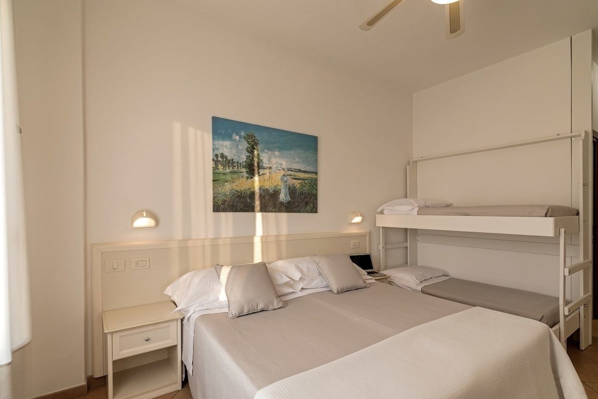 A bedroom with a bunk bed, a bedside table, a lamp, and a painting on the wall.