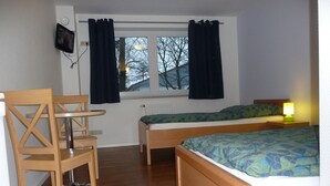 A room with two wooden beds, a wooden chair, a small table, a TV mounted on the wall, and a window with curtains. - Hotel Hansehus Süd (Hamburg)