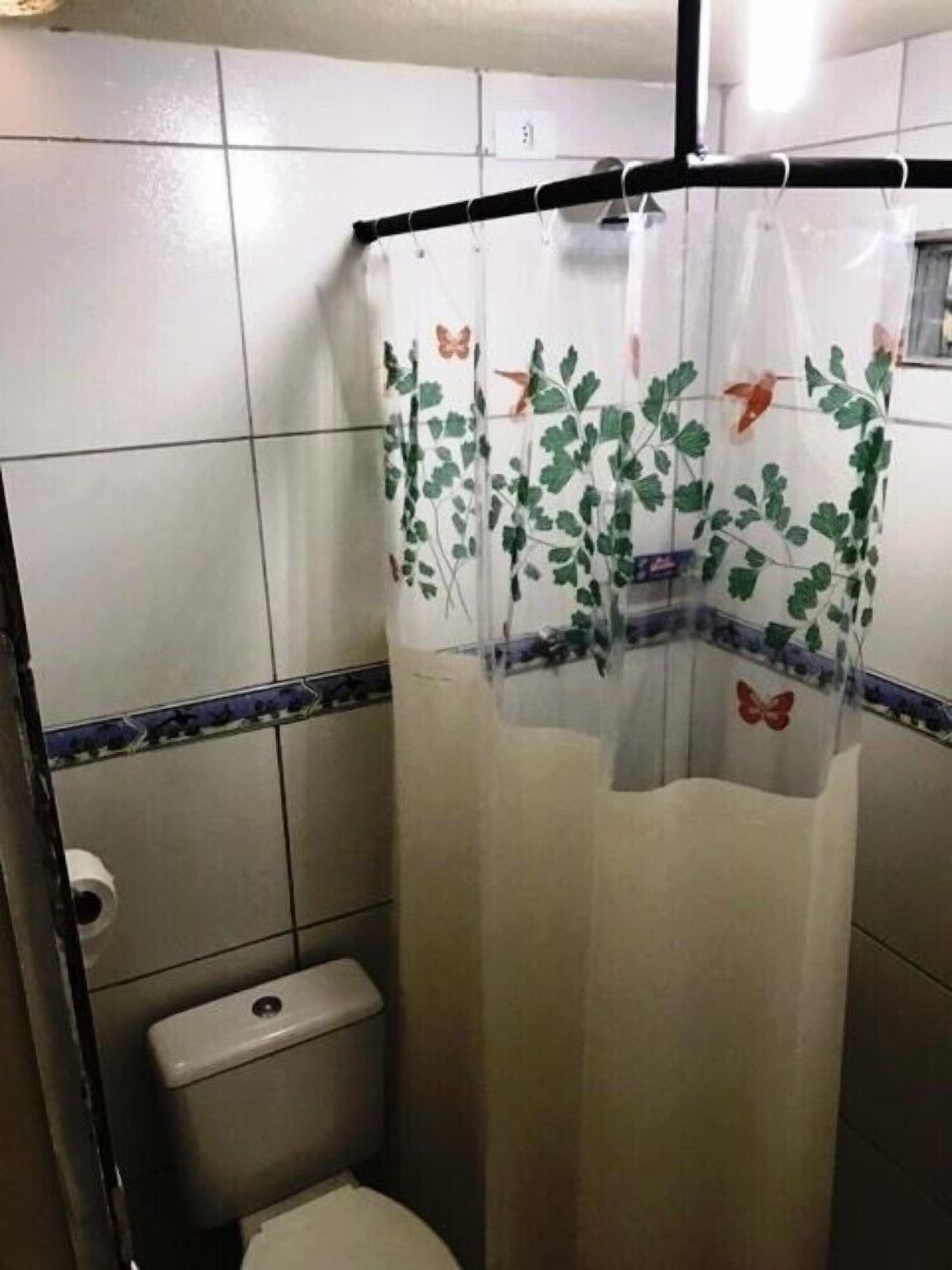 A bathroom with a toilet, a shower curtain with floral and butterfly patterns, and a tiled wall with a decorative border.