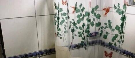 A bathroom with a toilet, a shower curtain with floral and butterfly patterns, and a tiled wall with a decorative border.