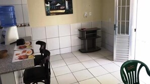 Una cocina pequeña con azulejos blancos, un cuadro en la pared, un dispensador de agua y una silla.