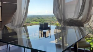 Un espace de repas moderne avec une table et des chaises en verre, de grandes fenêtres ornées de rideaux légers et une vue sur la campagne.