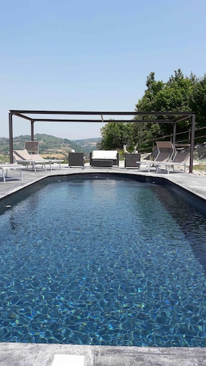 A swimming pool with clear water, surrounded by lounge chairs and a pergola. - CasaMatilda Agriturismo Langhe (Dogliani)