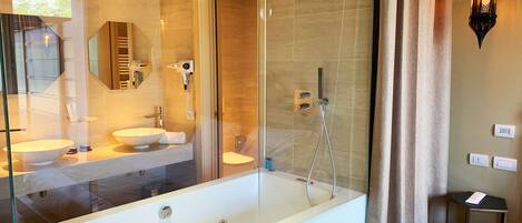 A modern bathroom with a glass-enclosed bathtub, a vanity with a large mirror, and a hairdryer on the wall.