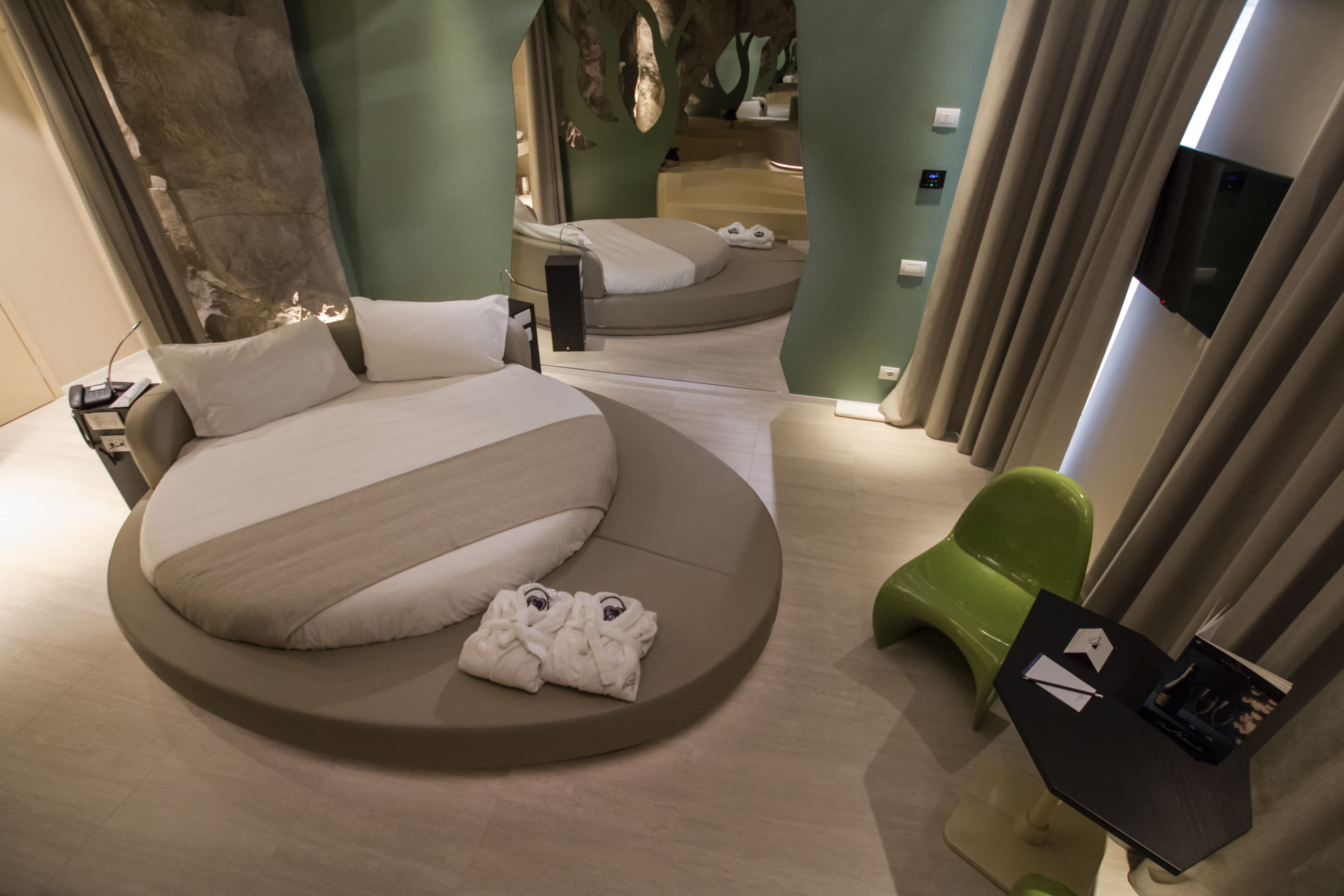 Ein modernes Hotelzimmer mit einem runden Bett, einem grünen Sessel und einem kleinen Tisch mit einer Fernbedienung.
