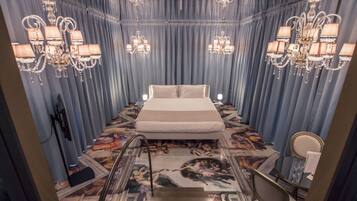Une chambre d’hôtel avec un grand lit, deux lustres, une table en verre avec une chaise et une fresque murale au sol.