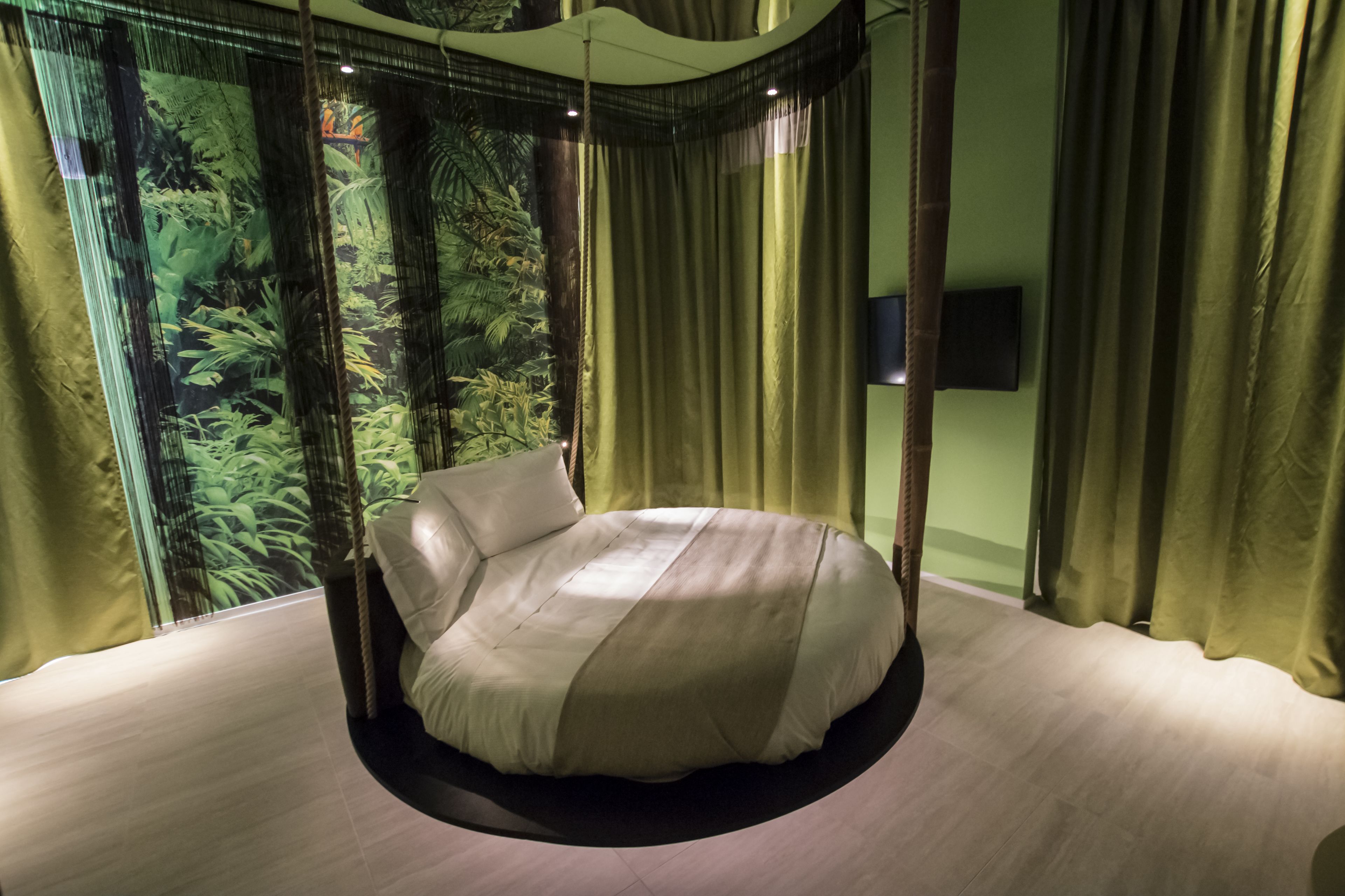 Una cama redonda en una habitación con vistas a una vegetación densa a través de cortinas translúcidas.