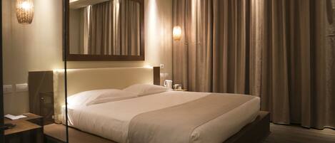 A modern hotel room with a large bed, bedside tables, a mirror, and a view of the curtains.