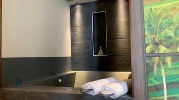 A modern bathroom with a large bathtub, a wall-mounted mirror, and a framed picture of a palm tree.
