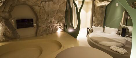 A spa room with a large bathtub, a sofa bed, and a television.