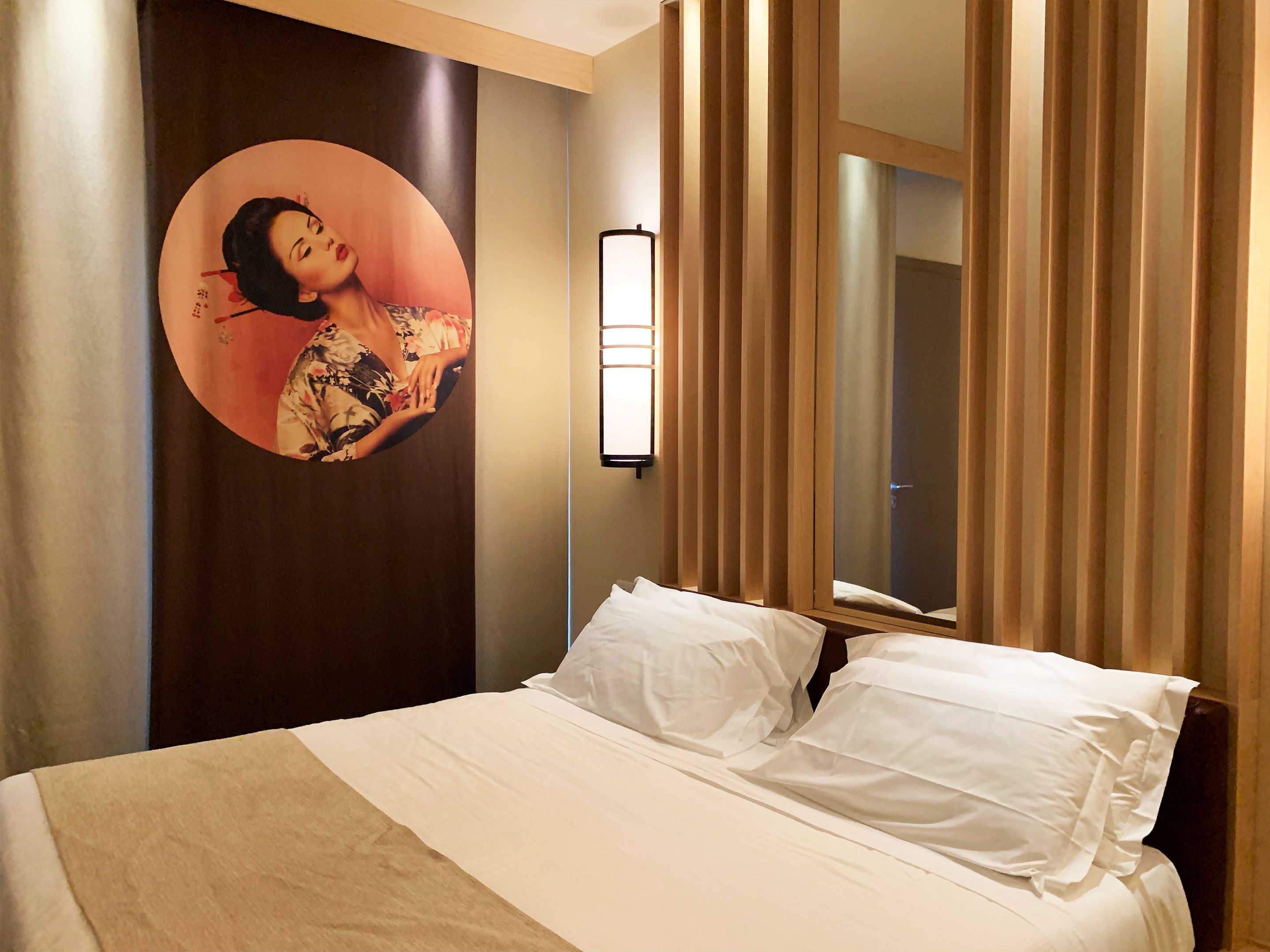 Ein Hotelzimmer mit einem Bett, einer Wandleuchte und einem großen Spiegel.