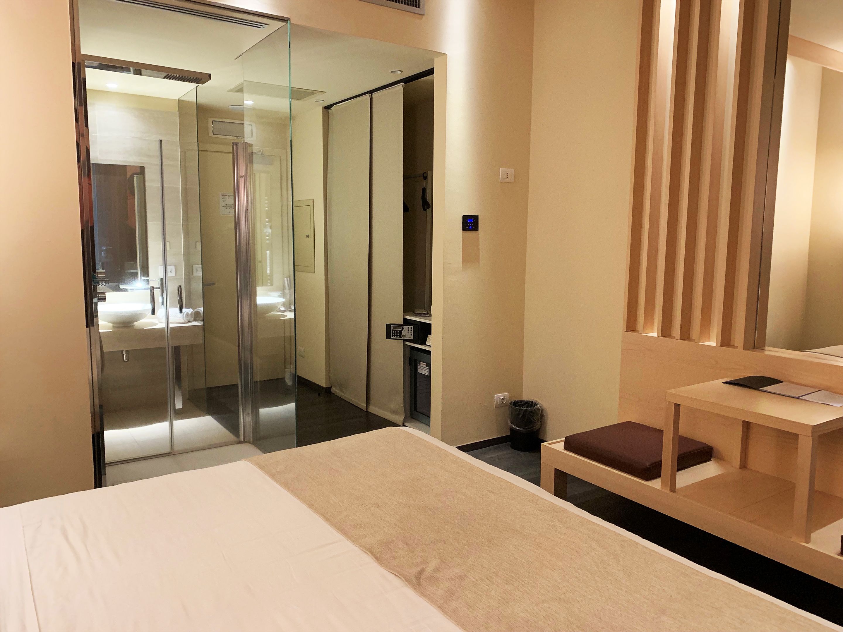 Una habitación de hotel con una cama, una mesita, un cubo de basura y un espejo.