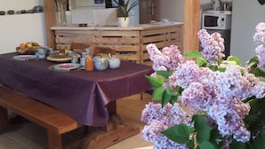 A dining area with a table set for four, wooden benches, a purple tablecloth, and a potted plant with purple flowers. - Au Pied du Figuier (Pauligne)