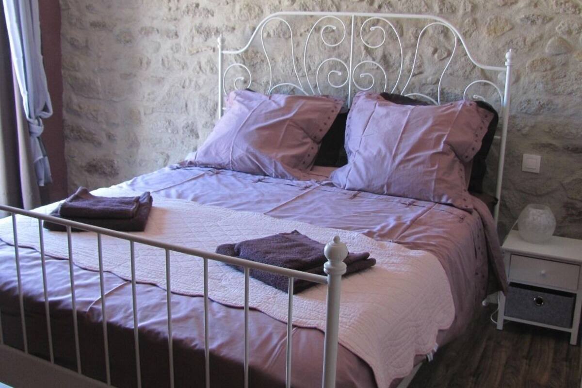 A bed with a metal frame, a stone wall behind it, and a nightstand with a lamp.