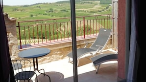 A balcony with a table and chairs, offering a view of a vineyard and rolling hills. - Au Pied du Figuier (Pauligne)