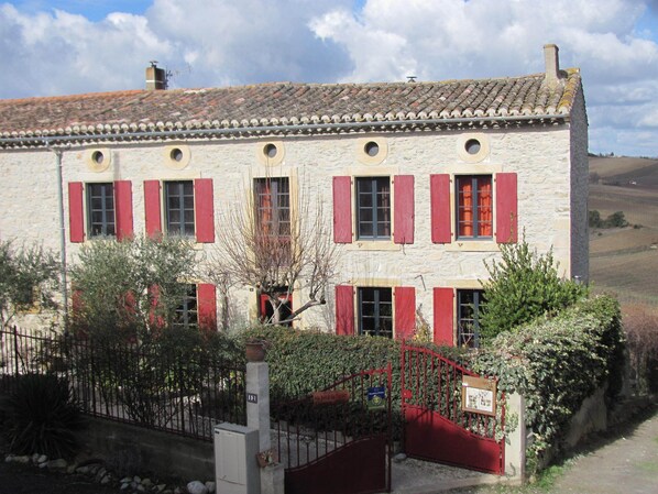 Un edificio de piedra con contraventanas rojas y tejado de tejas.