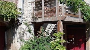 A rustic building with a wooden balcony, stone walls, and greenery. - Au Pied du Figuier (Pauligne)