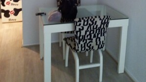 Een eethoek met een witte tafel en stoelen, een ronde spiegel aan de muur en een gestreept kussen op een stoel.