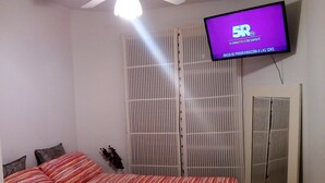 Een slaapkamer met een bed, een aan de muur bevestigde televisie, een plafondventilator en een kledingkast.