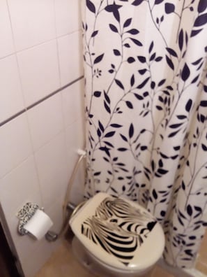 Um banheiro com vaso sanitário, um rolo de papel higiênico e cortina de chuveiro com padrão de folha.
