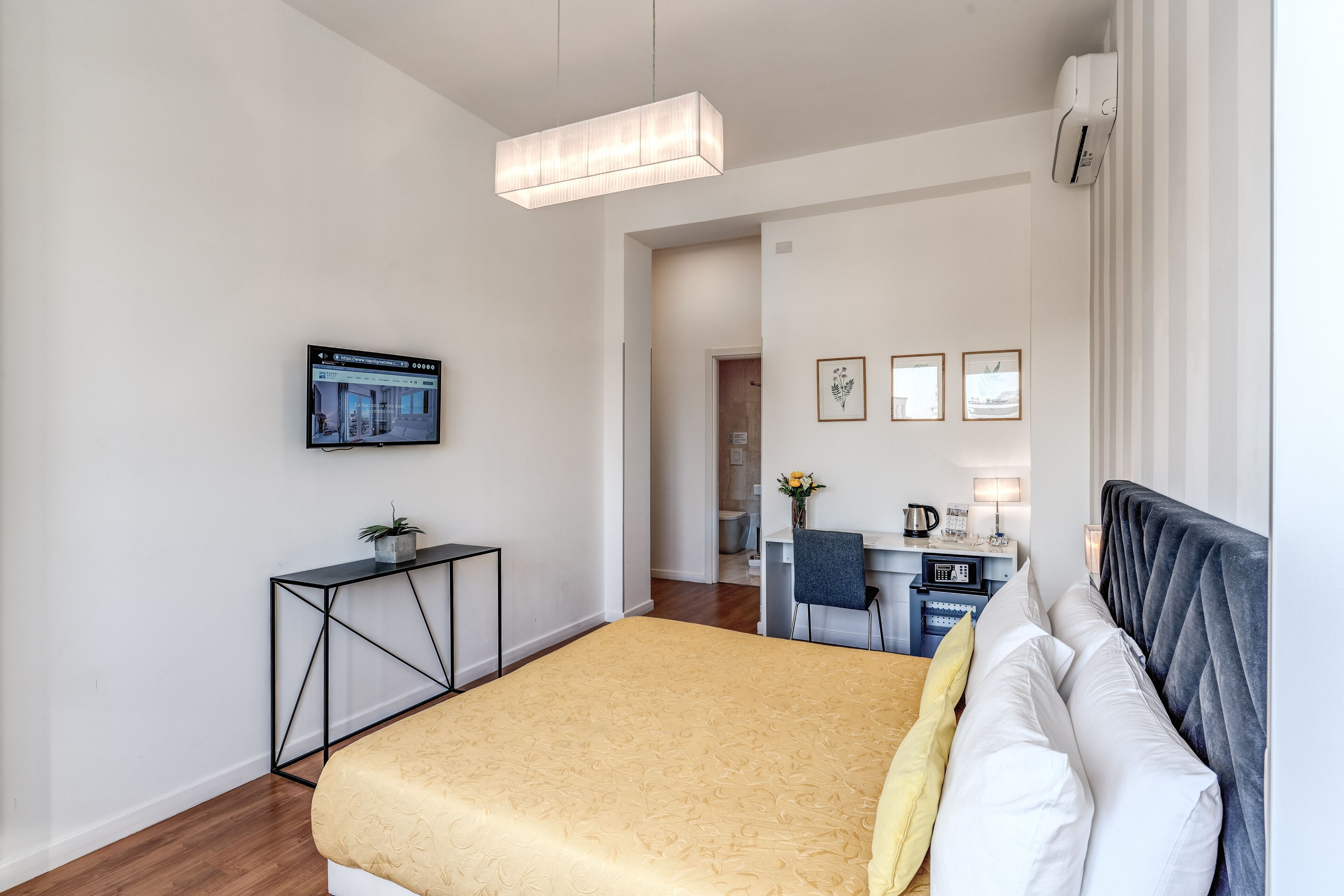 A modern hotel room with a large bed, a desk, and a television on the wall.