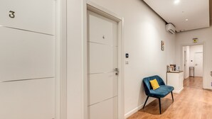 A hallway with white doors numbered 3 and 4, a blue chair with a yellow cushion, and a small kitchenette area. - Napoli Great View B&B (Naples)