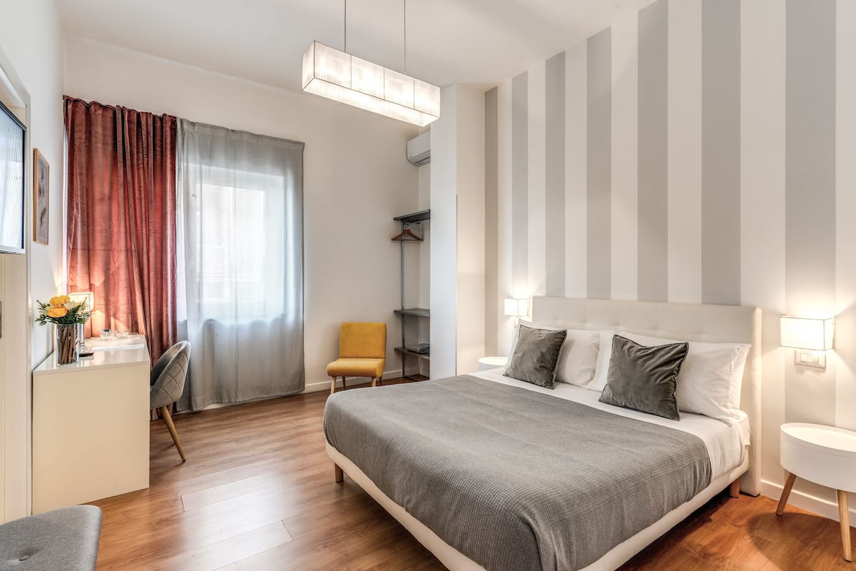 Et moderne soveværelse med en stor seng, et natbord, en stol og et skrivebord med lampe.