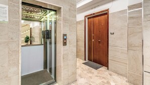 An elevator and a wooden door in a hallway with tiled flooring and marble walls. - Napoli Great View B&B (Naples)