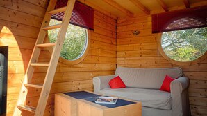 Interior acogedor de una cabaña con cama en altillo, un sofá con cojines rojos, una mesa de centro de madera y un tragaluz.