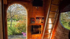 Interior acogedor de una cabaña con detalles de madera, una escalera, una mesita y un ventanal con vista a un jardín.