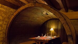 Una habitación circular de piedra con una mesa y bancos de madera, una lámpara y un suelo de baldosas.