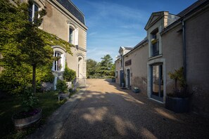 A gravel driveway leading to a building with a classic architectural style, surrounded by greenery and potted plants. - Carré d'Etoiles Paleine (Le Puy-Notre-Dame)