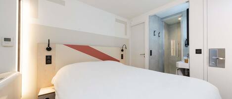 A modern hotel room with a large bed, a shower area, and a small bathroom.