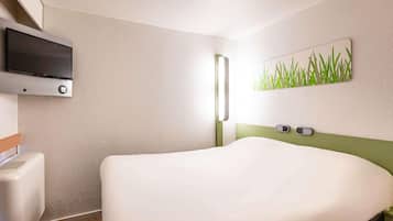 Una habitación de hotel con una cama, un televisor montado en la pared, un reloj de pared y un cuadro con paisaje de hierba.