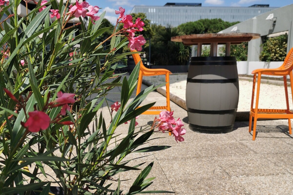 An outdoor seating area with orange chairs, a round table, and a potted plant with pink flowers.