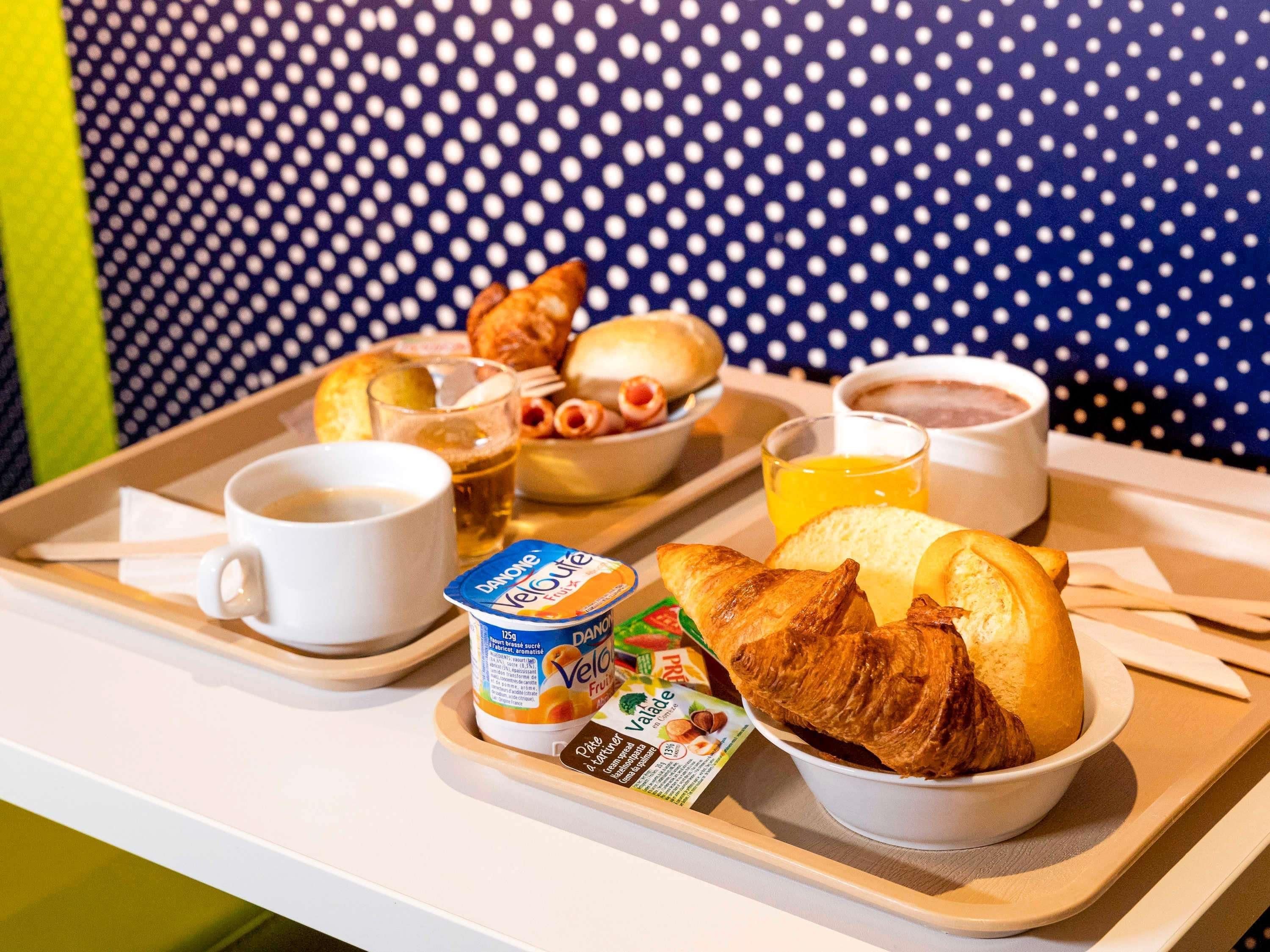 A tray with breakfast items including croissants, a bowl of fruit, a cup of coffee, and a glass of orange juice.