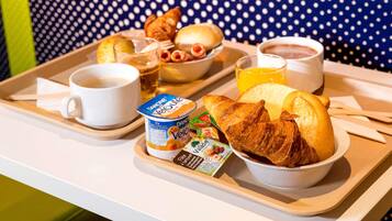 A tray with breakfast items including croissants, a bowl of fruit, a cup of coffee, and a glass of orange juice.
