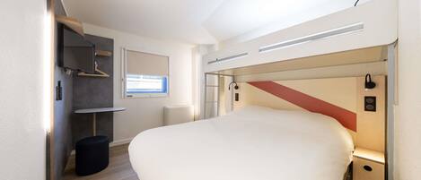 A modern bedroom with a large bed, a small desk, a chair, a wardrobe, and a window.