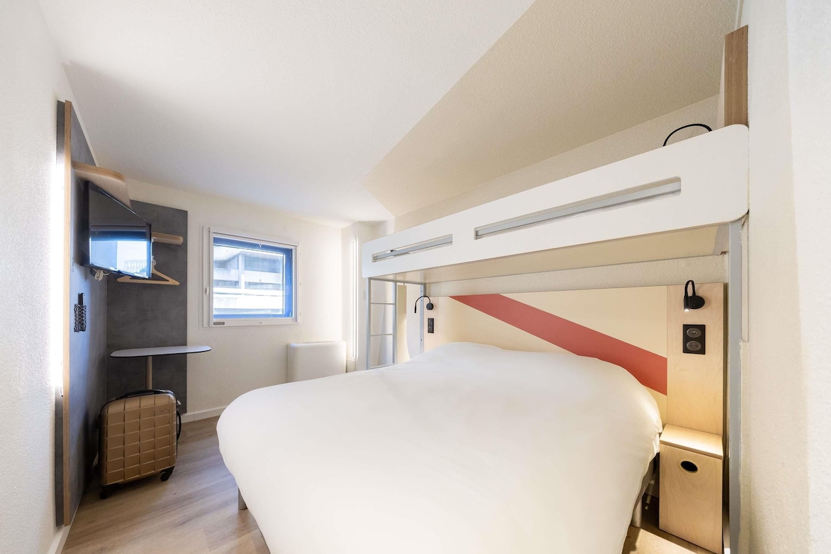 A compact room with a bunk bed, a small desk, a chair, and a suitcase.