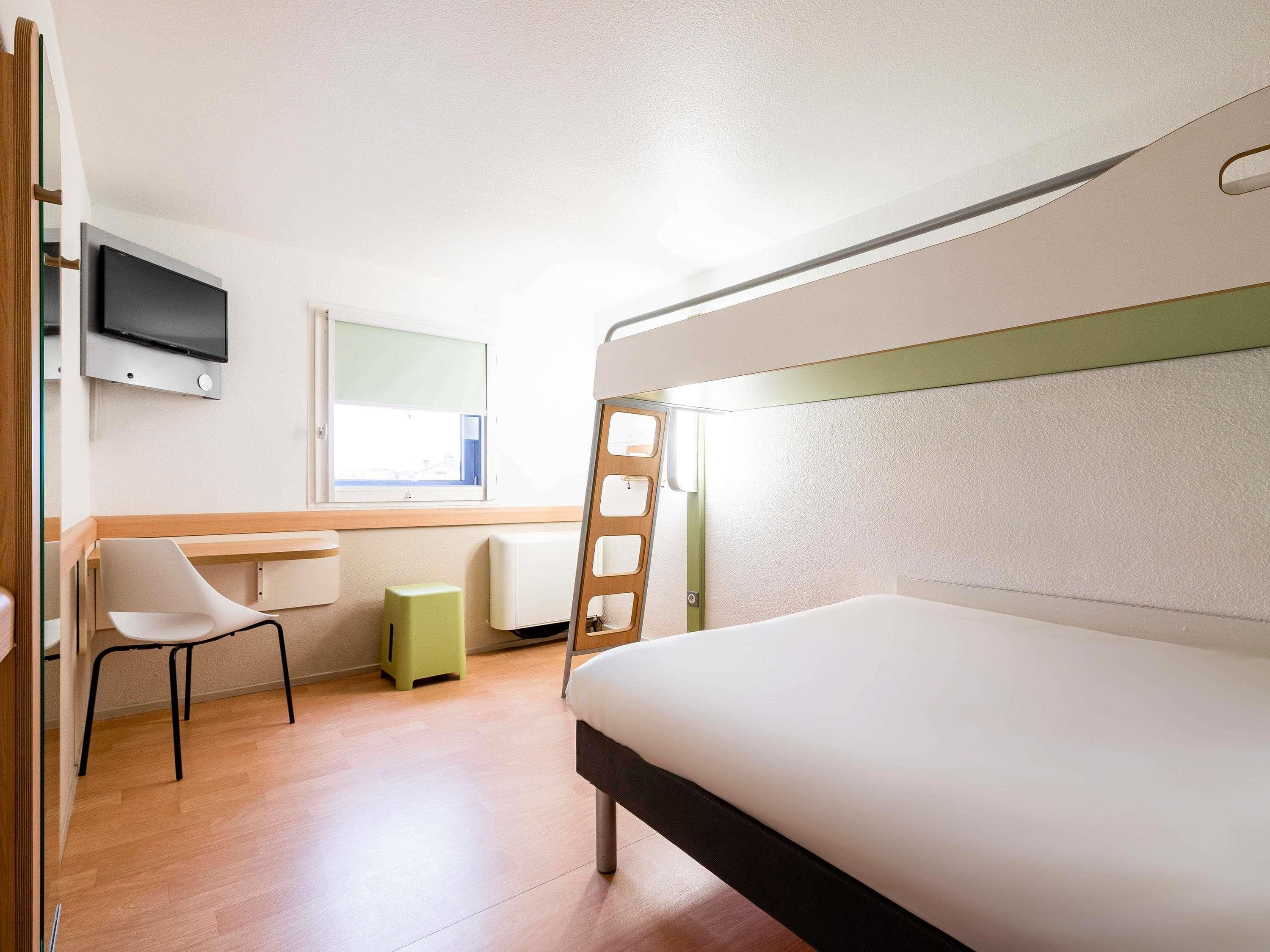 Une chambre avec un lit superposé, une télévision, un bureau, une chaise et une échelle.