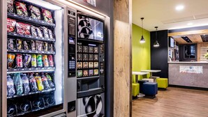 A vending machine with snacks and beverages, a wooden accent wall, and a seating area with yellow chairs. - ibis budget Bordeaux Centre Mériadeck (Bordeaux)